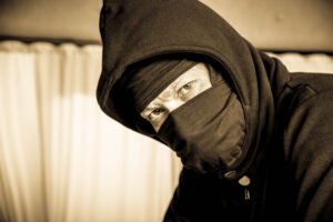 Masked man in dark clothing, representing a scammer